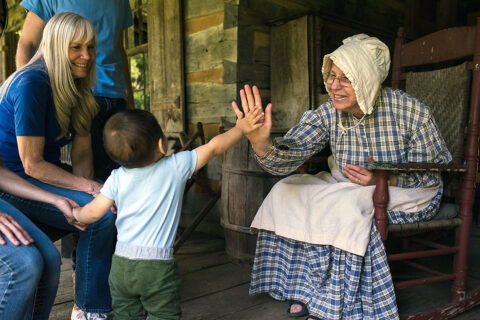 Child shares a high-five with a docent on the steps of a house at Historic Collinsville Pioneer Settlement. 